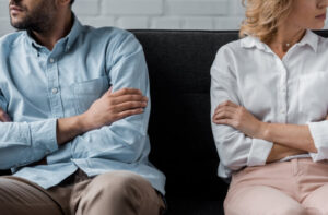 A man and woman with arms crossed on a couch due to one of the top 3 reasons for divorce