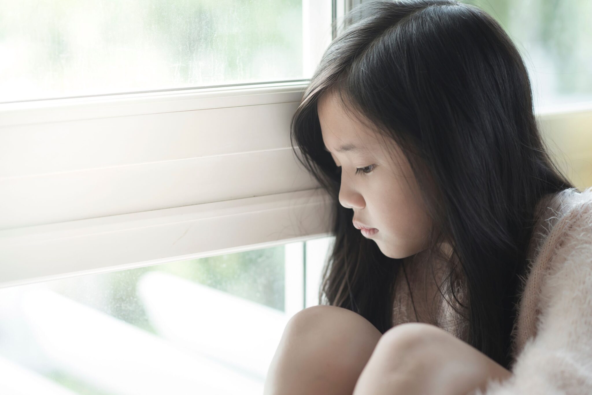 A young child sits by a window, reflecting on the emotional impact of high-conflict divorce on mental health and family dynamics