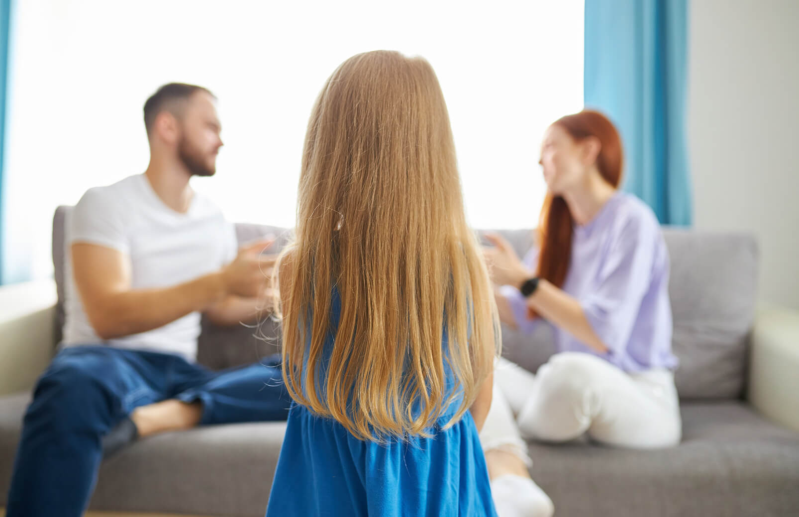 Child standing in the foreground while parents argue on a couch in the background.