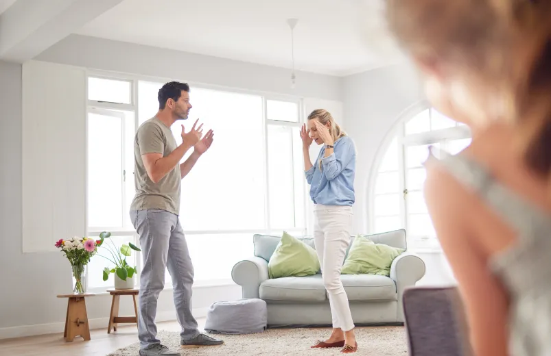 Parents arguing in the living room while a child observes.