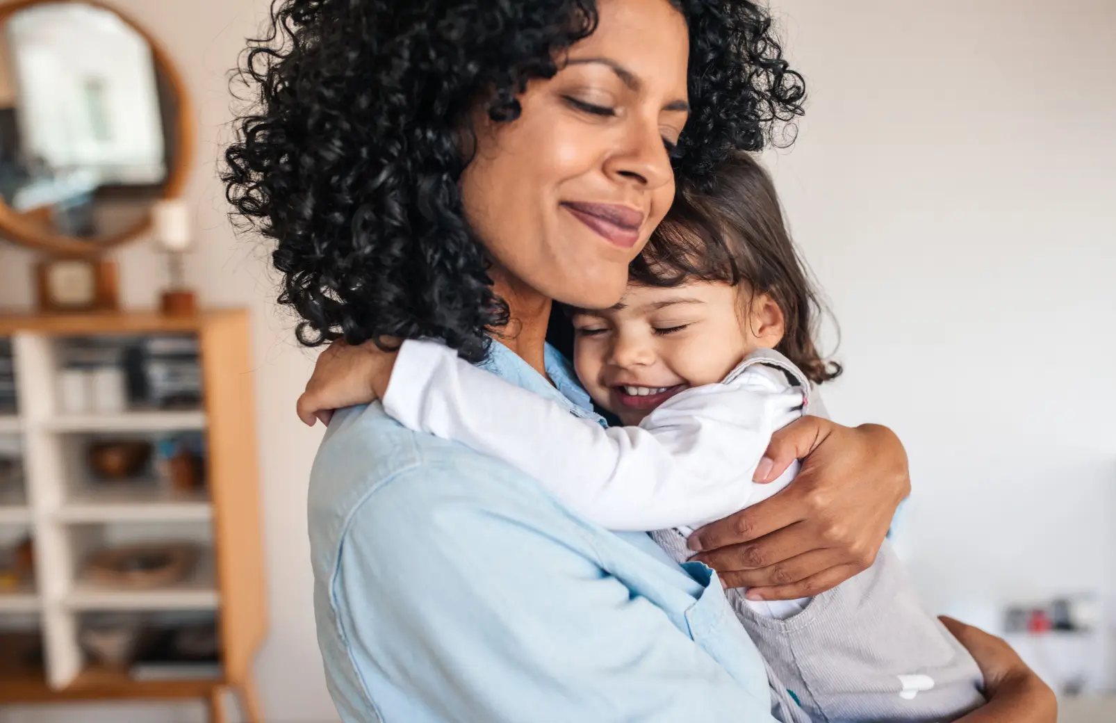 Mother smiling with eyes closed while embracing her young child at home, showing what emotional safety looks like for kids