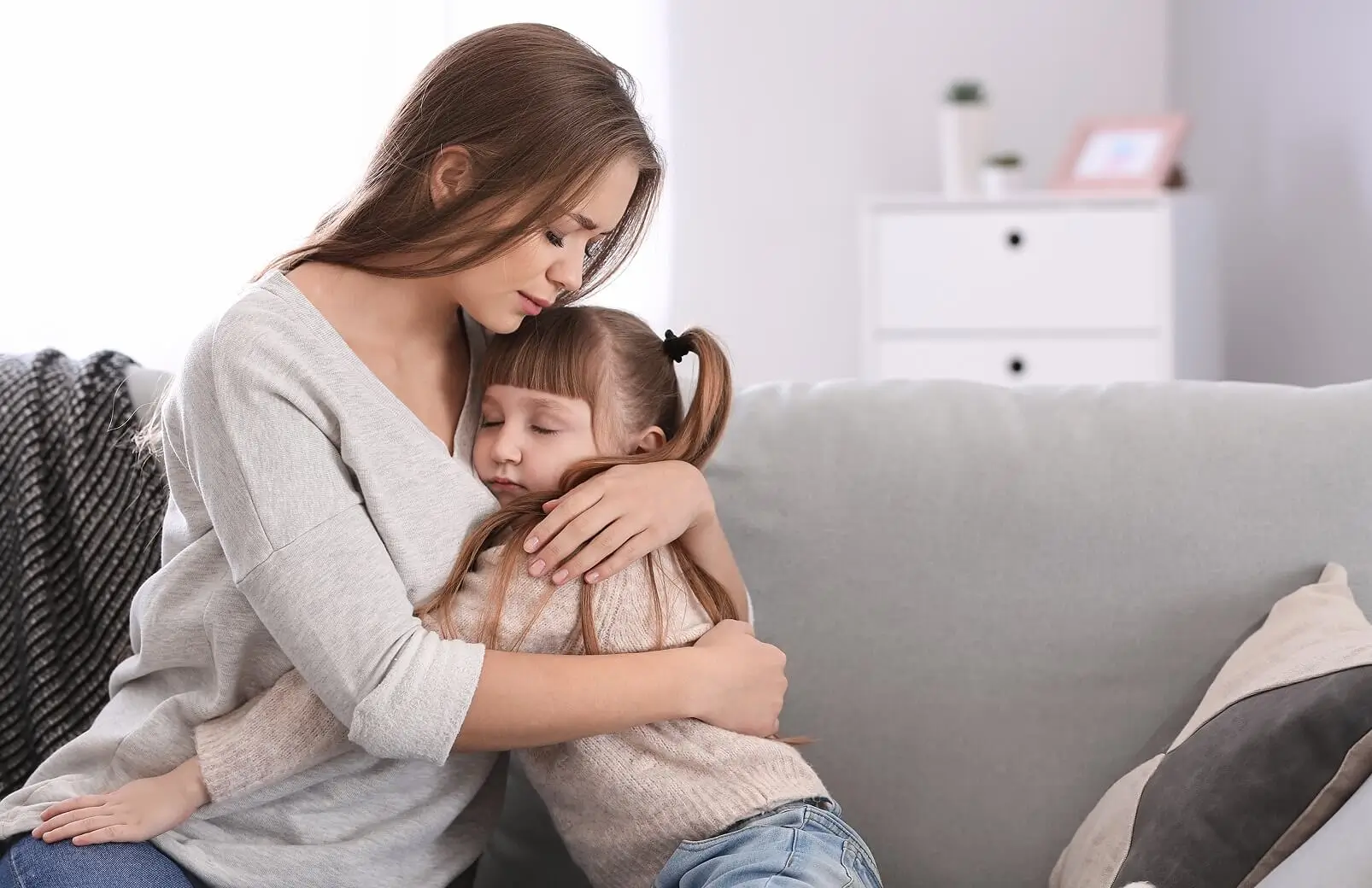 A mother hugging her young daughter on a sofa, offering comfort and support after a divorce