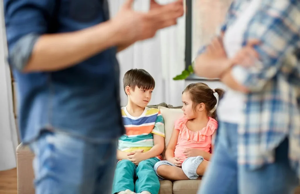 Two sad children sitting together at home while their parents argue, illustrating the signs a child may be struggling after a divorce