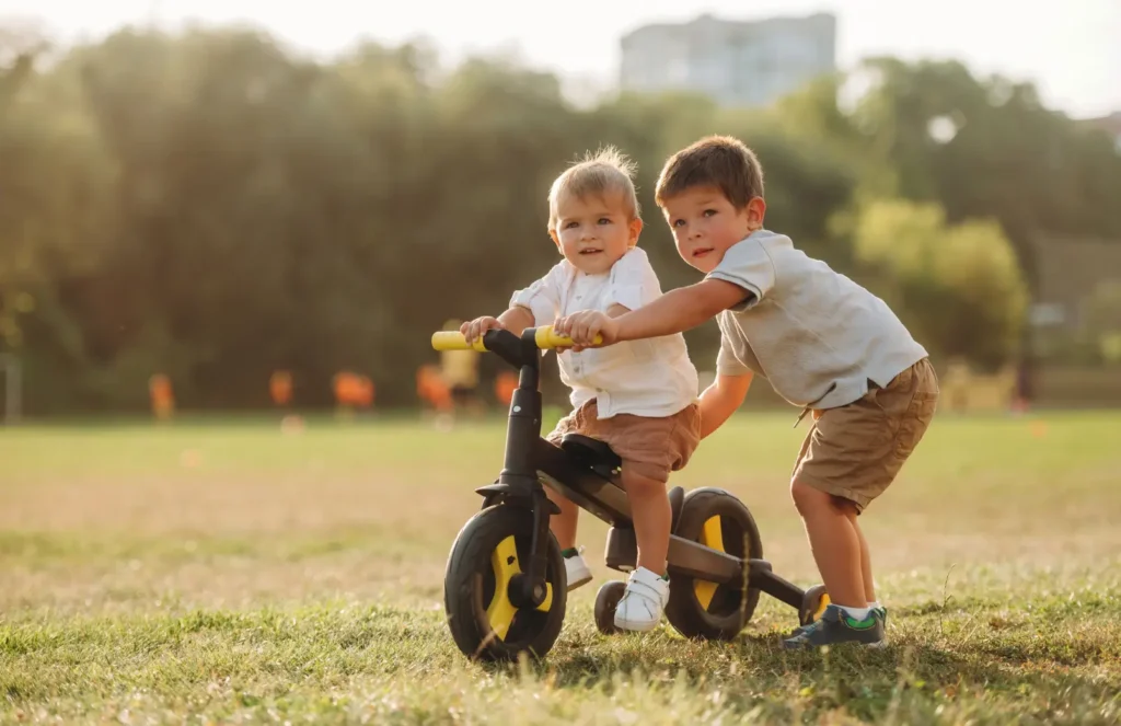 Two young brothers playing together outside on a balance bike on a sunny summer afternoon