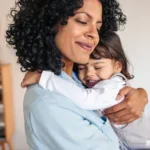 Mother smiling with eyes closed while embracing her young child at home, showing what emotional safety looks like for kids